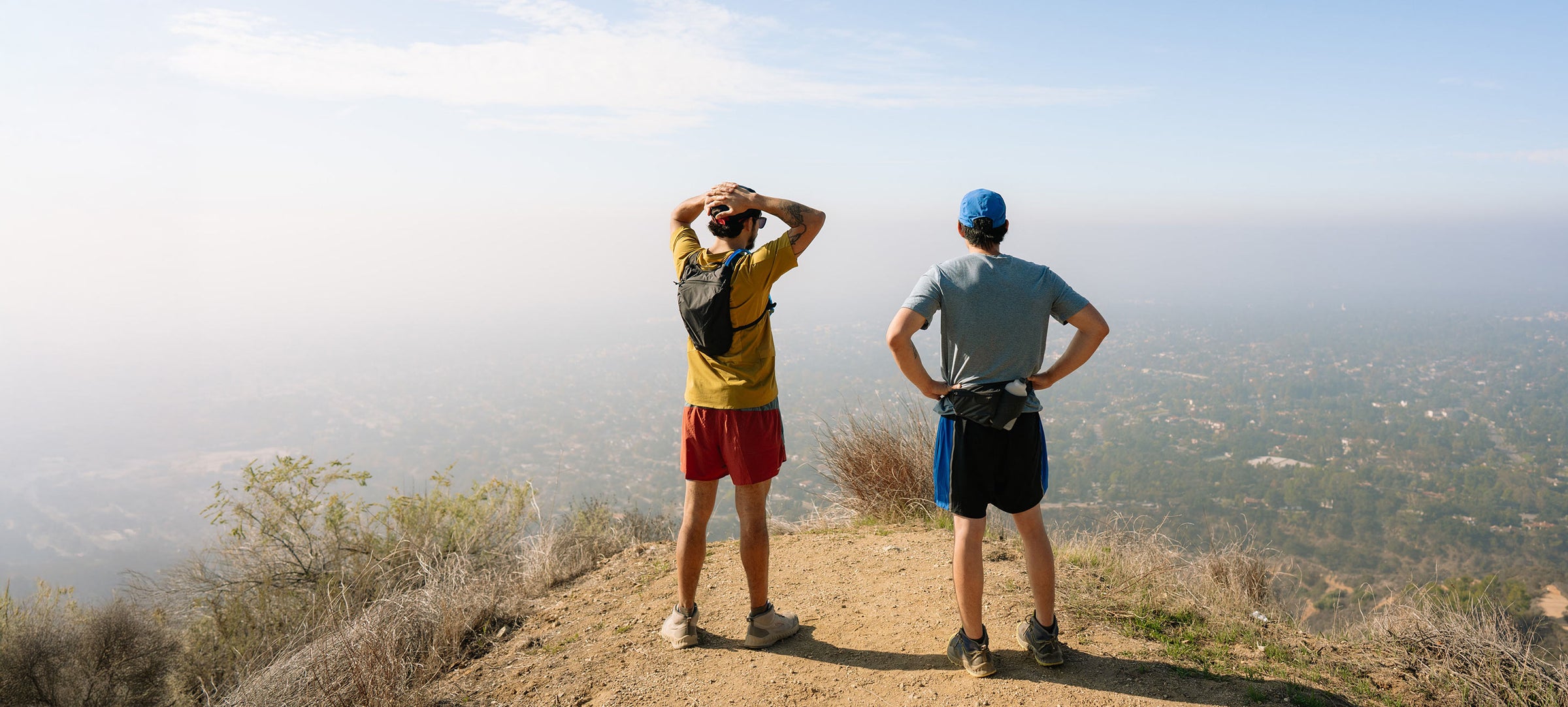Two people standing on a hilltop, looking out over a scenic landscape.