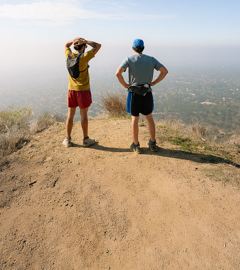Two people standing on a dirt path overlooking a scenic landscape.