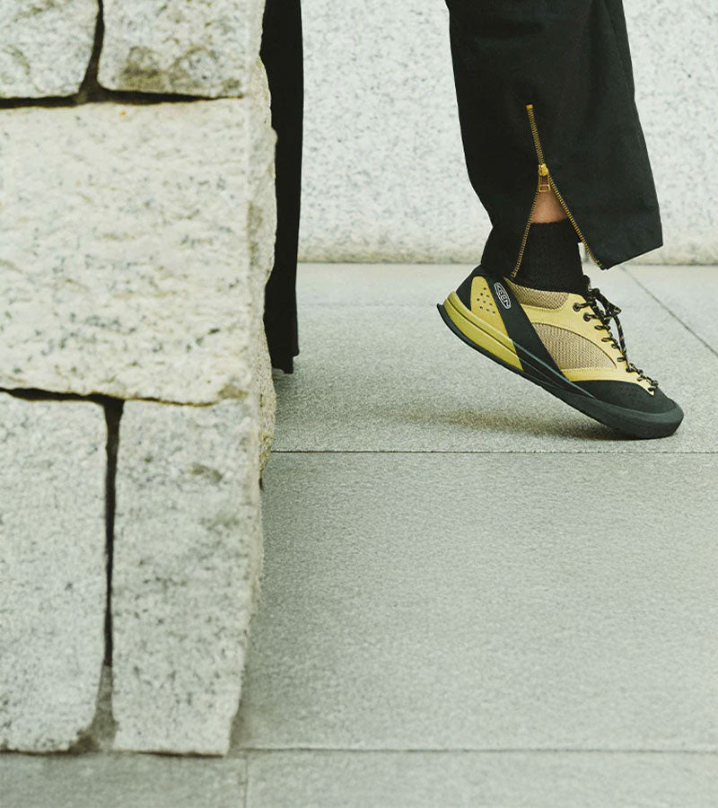 Person wearing yellow and black shoes stepping onto a stone surface.