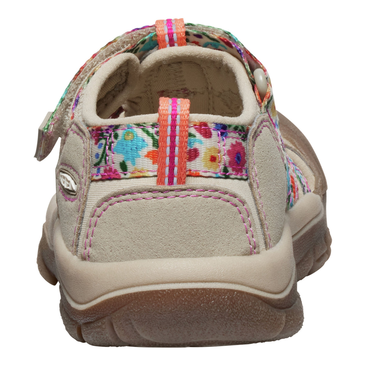 A children's casual shoe shown from the side profile on a white background. The upper is primarily beige suede with a colourful floral patterned strap and pull tab, pink stitching, and a brown rubber sole.
