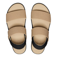 A pair of minimalist slide sandals shown from a top-down view on a white background. The sandals feature a beige woven upper with a black elastic ankle strap and a beige footbed.