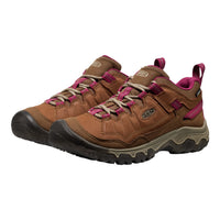 A pair of Keen mid-height hiking shoes in brown leather with vibrant pink accents, beige laces, and black soles, shown on a plain white background.