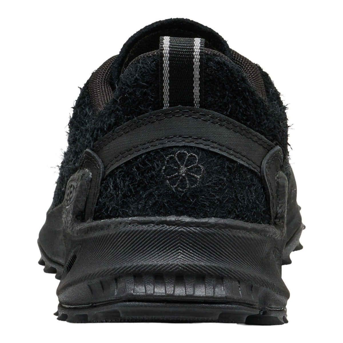 A close-up rear view of a black outdoor shoe with a fuzzy fleece upper, textured synthetic back strap, and a small embroidered flower logo on the heel.
