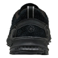 A close-up rear view of a black outdoor shoe with a fuzzy fleece upper, textured synthetic back strap, and a small embroidered flower logo on the heel.