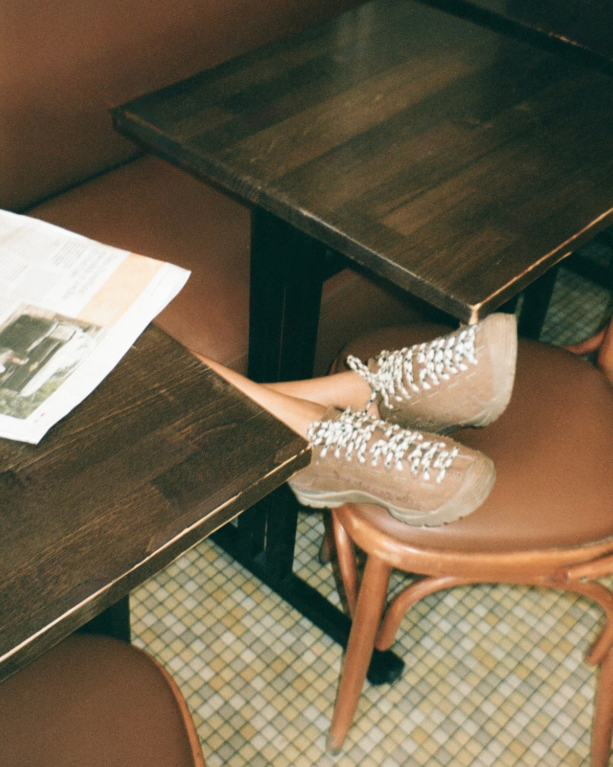 A person's legs crossed over a dark wood table in a cafe setting, wearing beige lace-up boots with white laces.