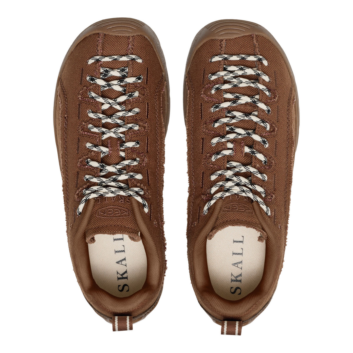 A pair of brown suede low-top sneakers shown from a top-down view, featuring braided white and black laces and the SKALL brand name printed on the cream-colored insoles.