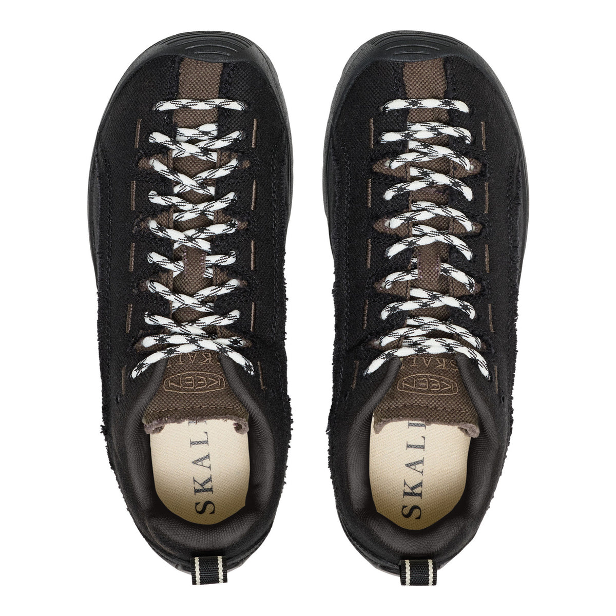 A pair of black suede and mesh low-top sneakers with white braided laces, shown from a top-down view on a white background. The interior lining is beige with the brand name 'SKAL' printed on it.