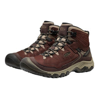 A pair of Keen mid-cut hiking boots in dark brown and beige, featuring black laces and a rugged sole, shown against a plain white background.