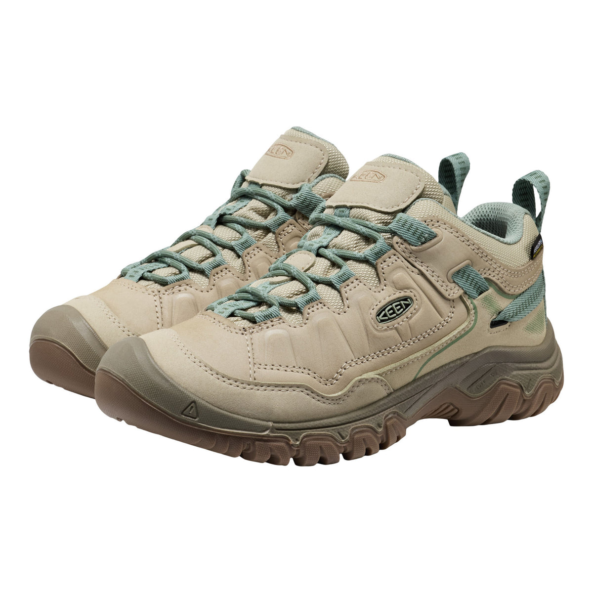 Pair of beige hiking shoes with green laces on a white background