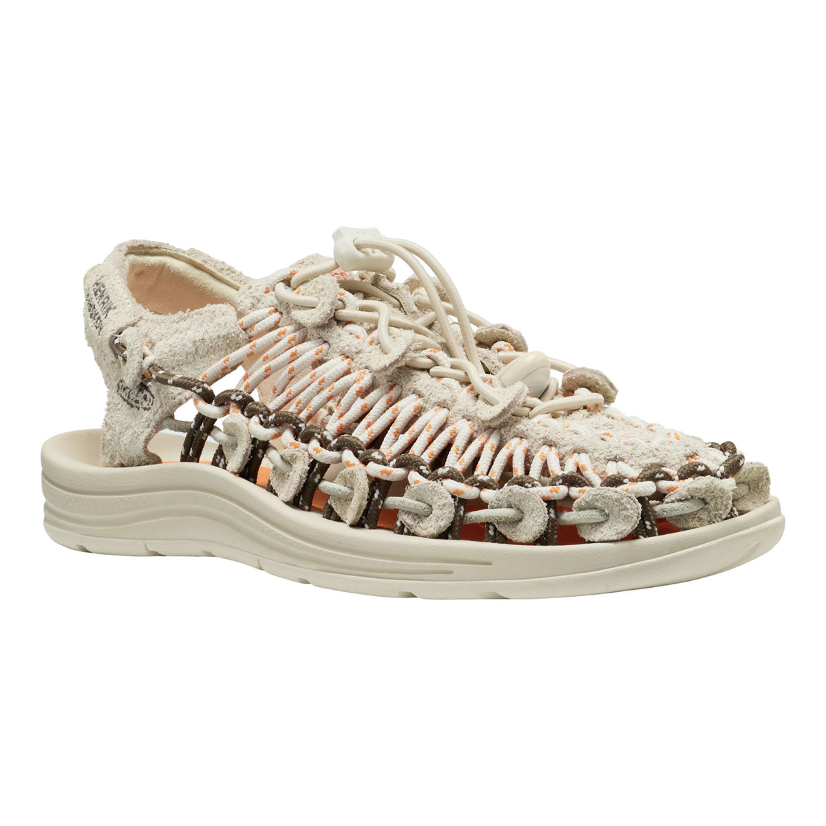 A woven lace-up sandal with a chunky off-white sole, featuring textured beige straps, orange-brown braided accents, and a white footbed, shown on a plain white background.