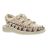 A woven lace-up sandal with a chunky off-white sole, featuring textured beige straps, orange-brown braided accents, and a white footbed, shown on a plain white background.