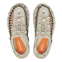 A pair of KEEN brand slip-on shoes shown from a top-down view against a white background. The shoes feature a cream-colored woven upper with orange and dark brown accents, and a bright orange insole.