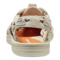 Sandal in a textured beige suede-like material with silver-tone metal studs and a thick beige sole, shown against a plain white background.