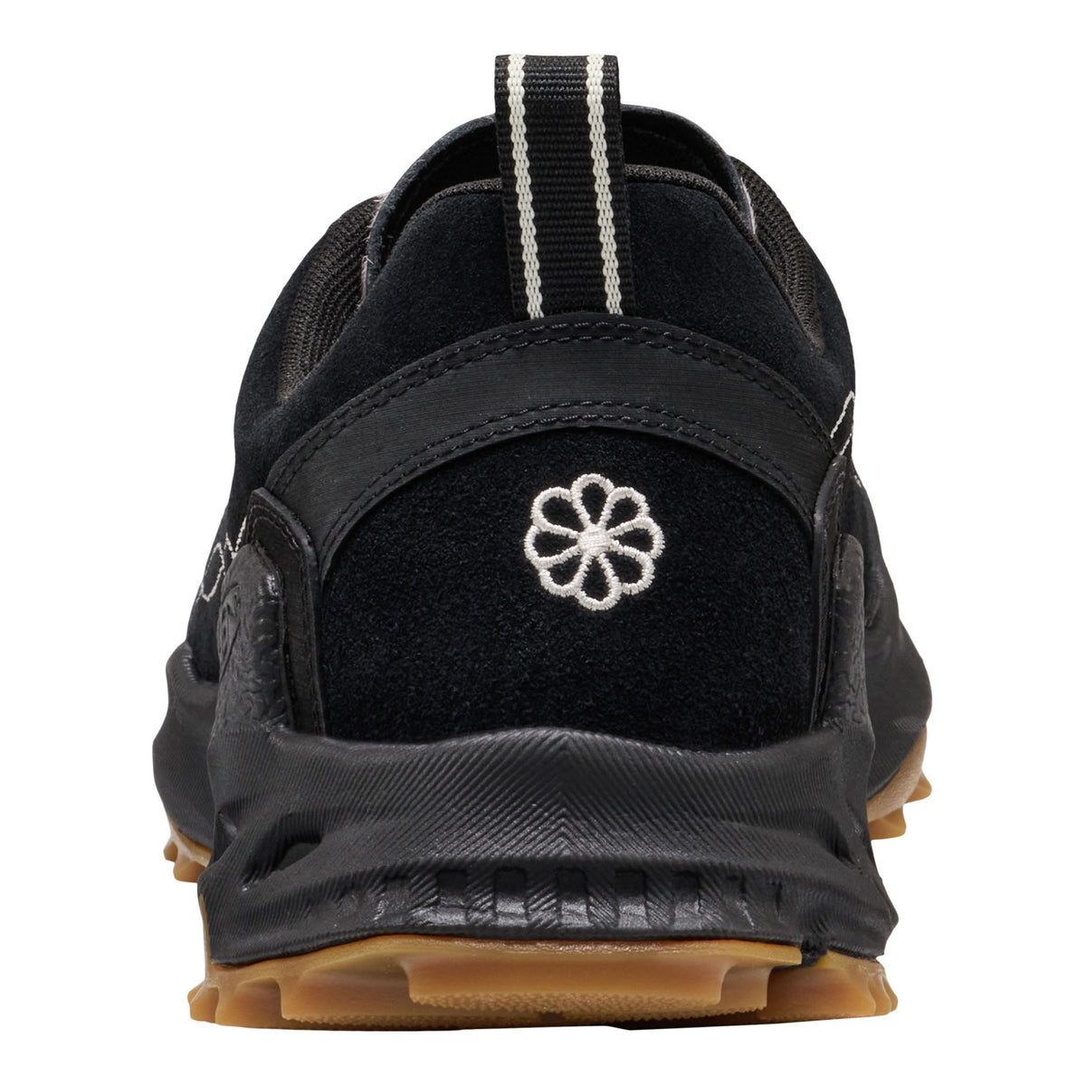 A close-up rear view of a black athletic shoe with a white embroidered flower logo on the heel, a black and white striped pull tab, and a brown gum outsole, shown against a plain white background.