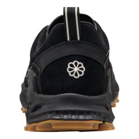 A close-up rear view of a black athletic shoe with a white embroidered flower logo on the heel, a black and white striped pull tab, and a brown gum outsole, shown against a plain white background.