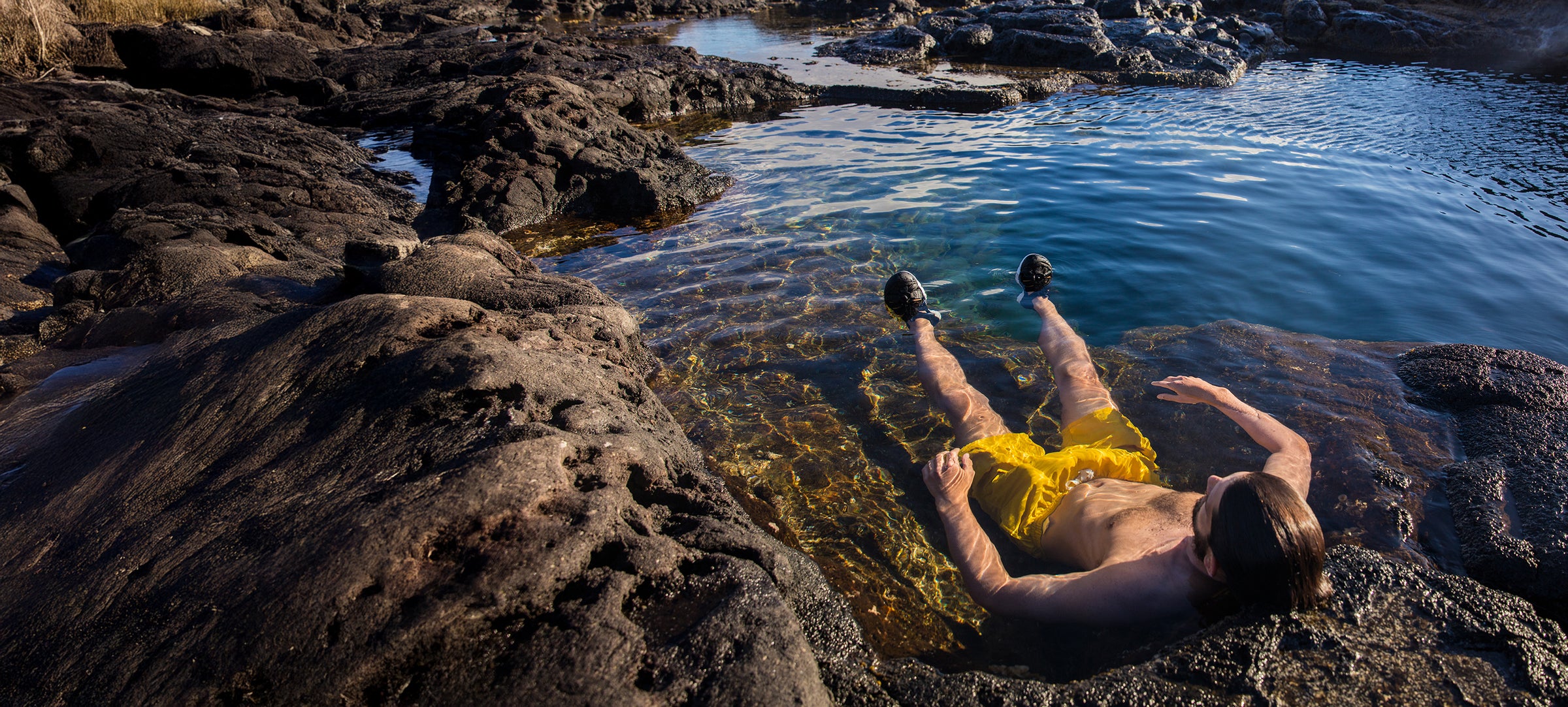 Person lying on rocks by a pool of water with yellow shorts