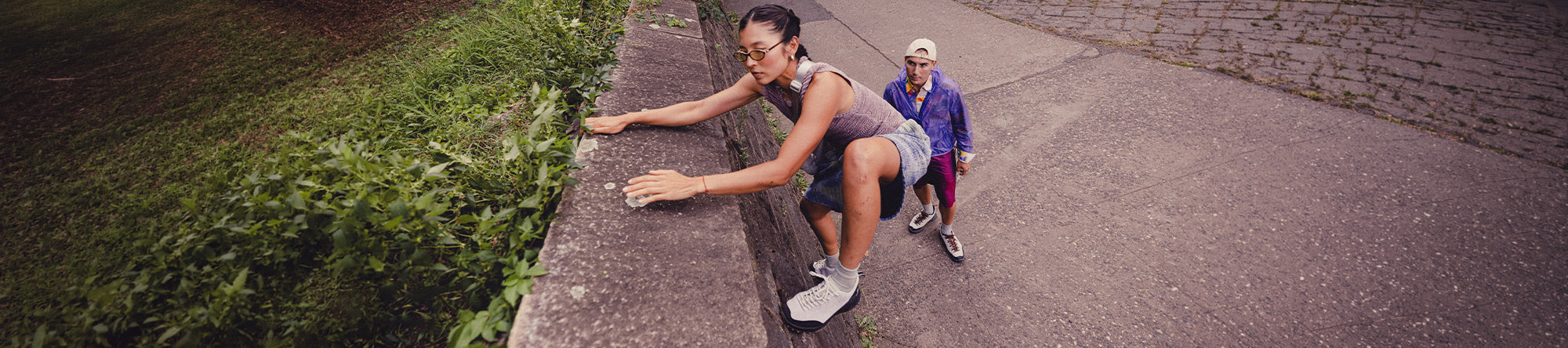 Two people running on a path with grass and a wall in the background
