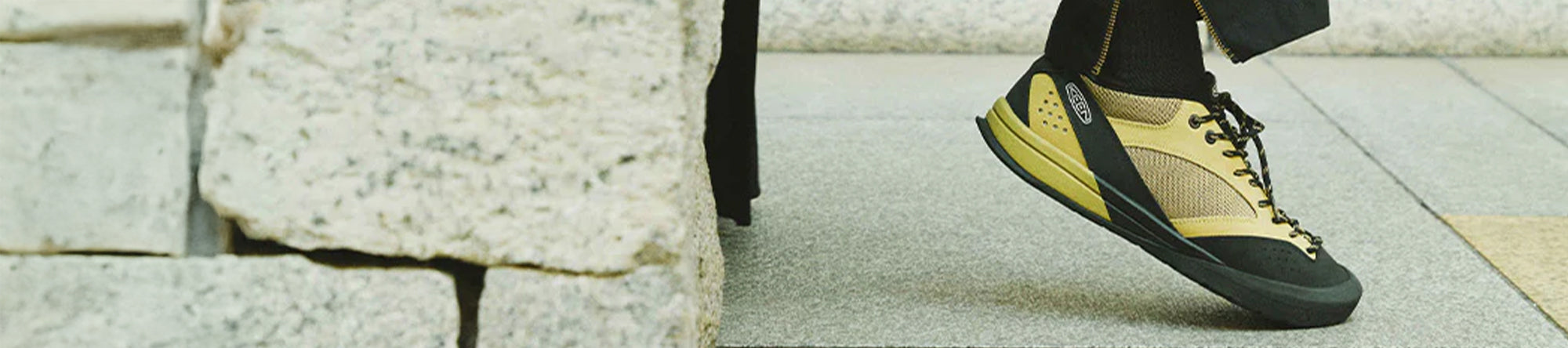 Person wearing yellow and black sneakers walking on a stone pavement.