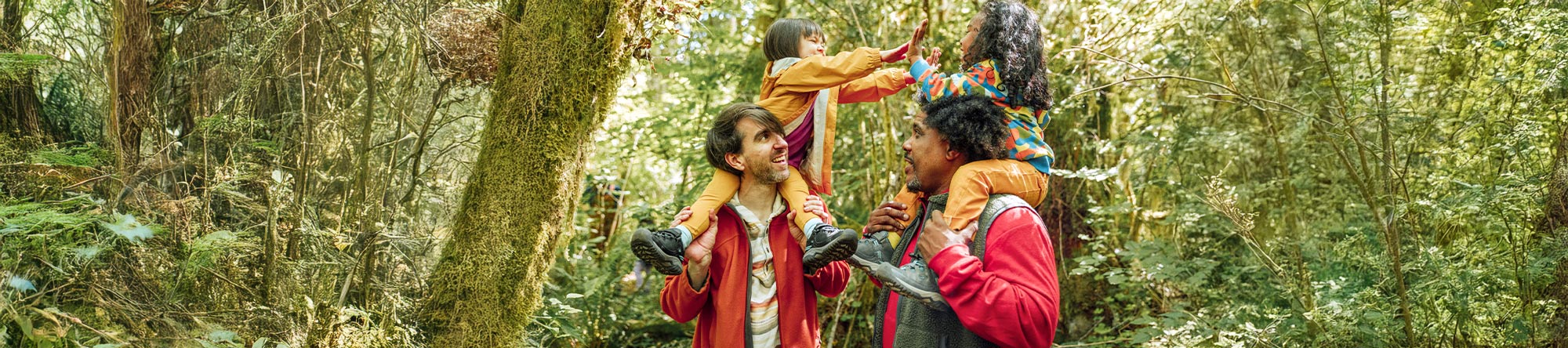Two people with children on their shoulders in a forest setting