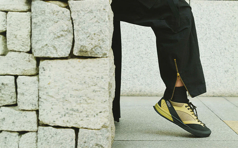 Person wearing black shoes with yellow accents against a stone wall background