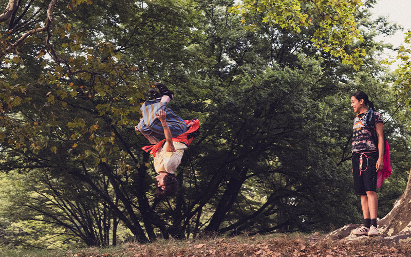 Person performing a backflip in a park with another person watching.