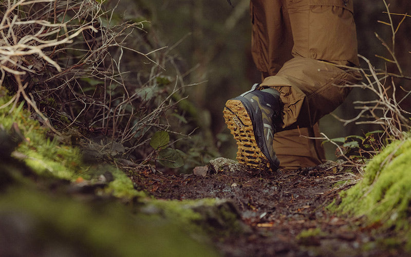 Person walking on a forest path wearing hiking boots with a focus on the boots and surrounding greenery.