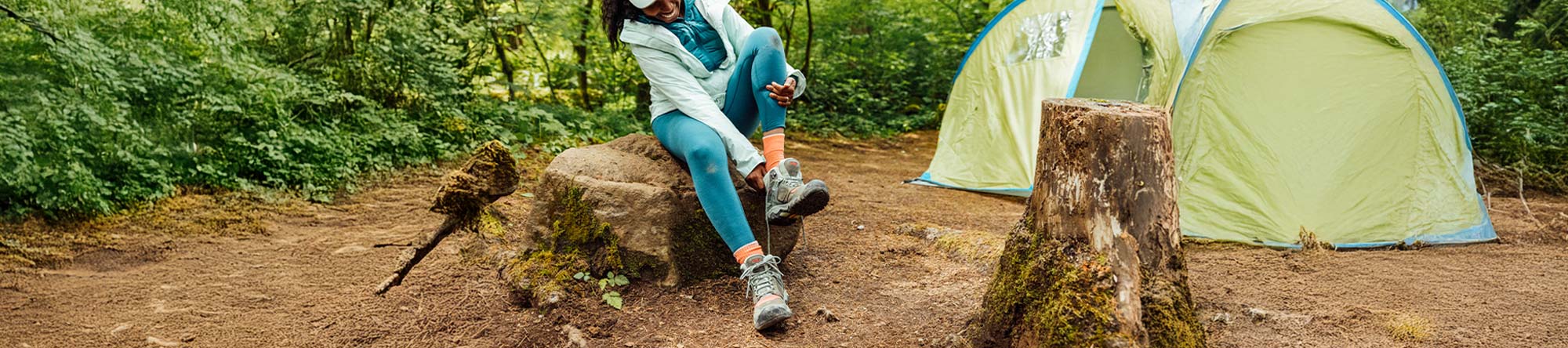 Person sitting on a rock near a tent in a forest setting