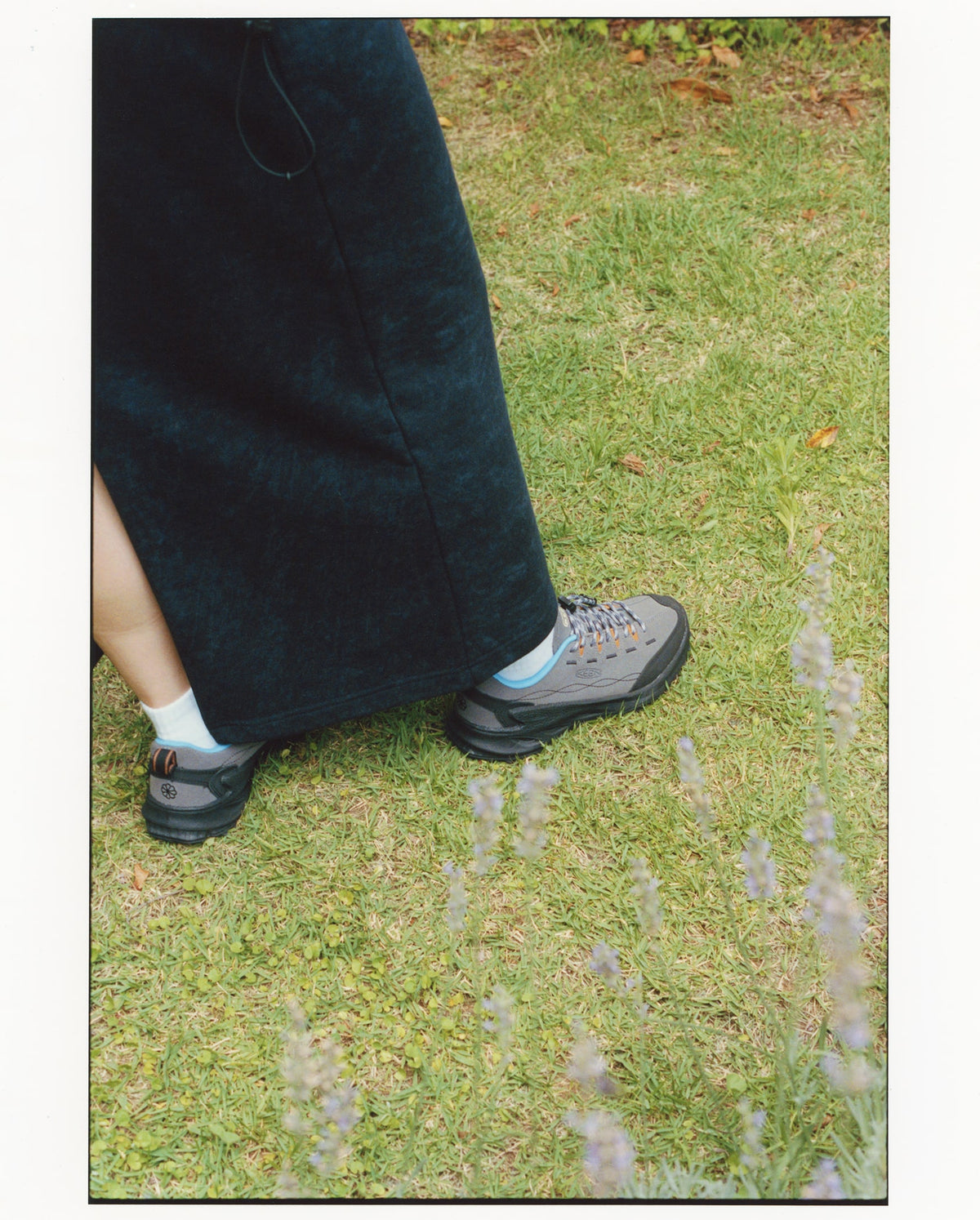 Person wearing a dark black skirt and grey shoes on grass