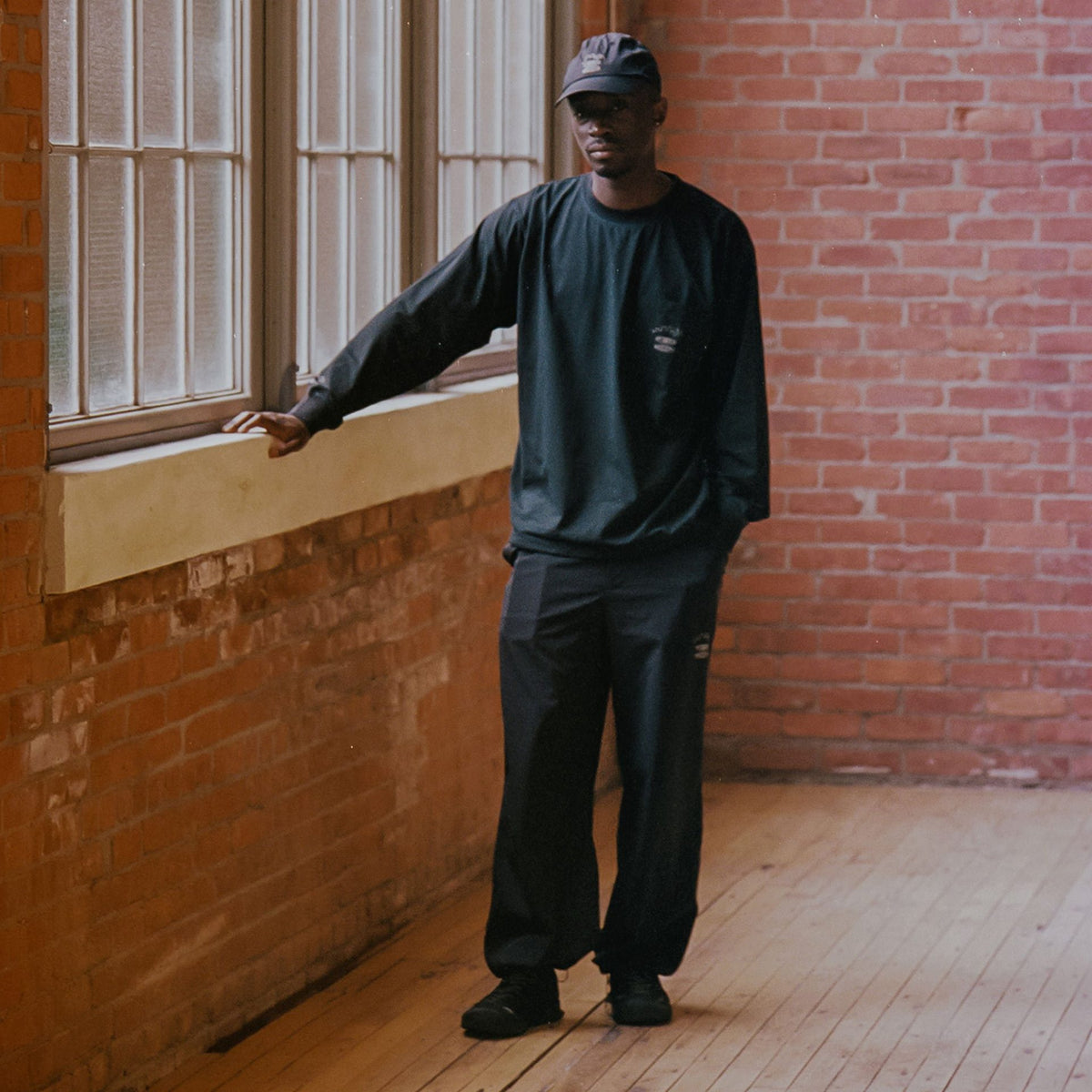 Man in dark clothing standing in a room with brick walls and wooden floor.