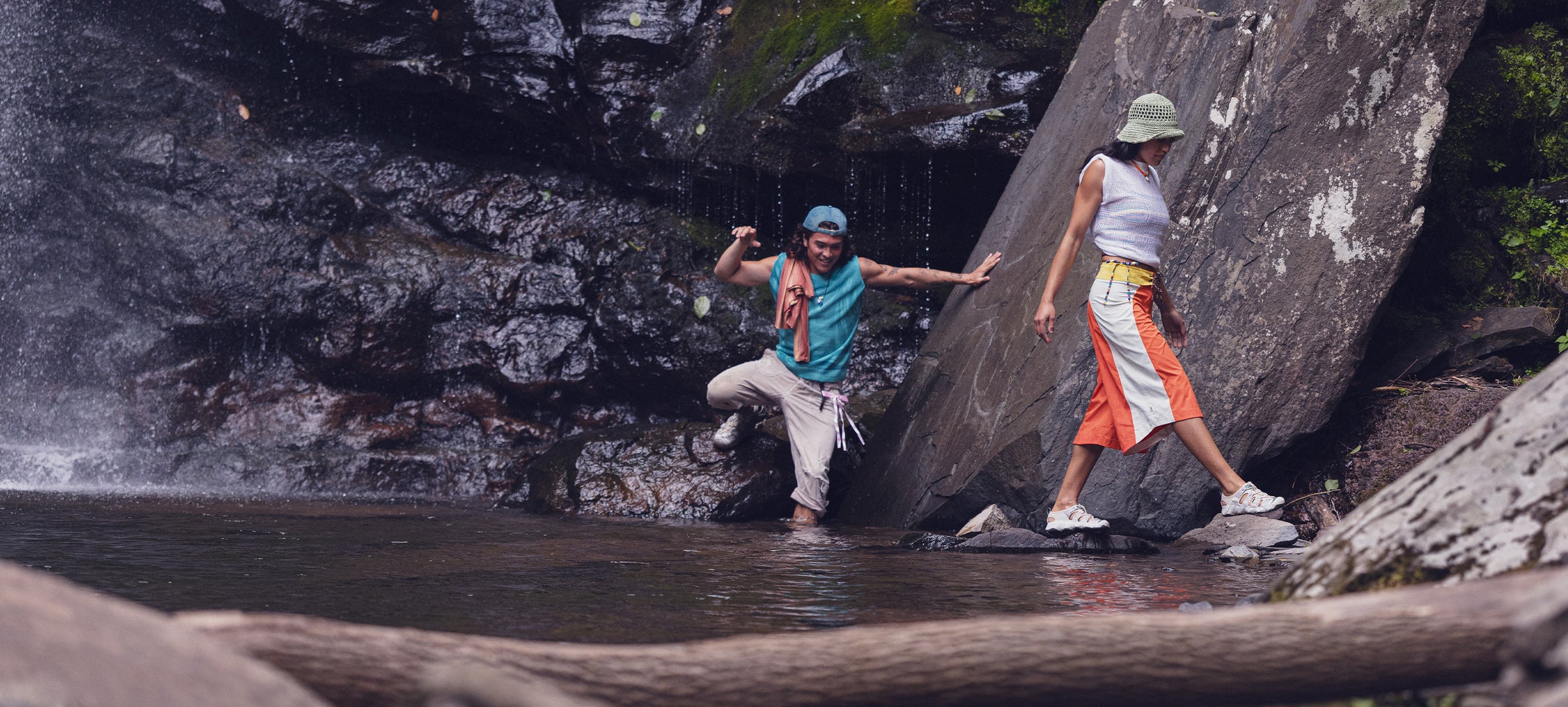 Two people standing near a waterfall with rocks and water around them.