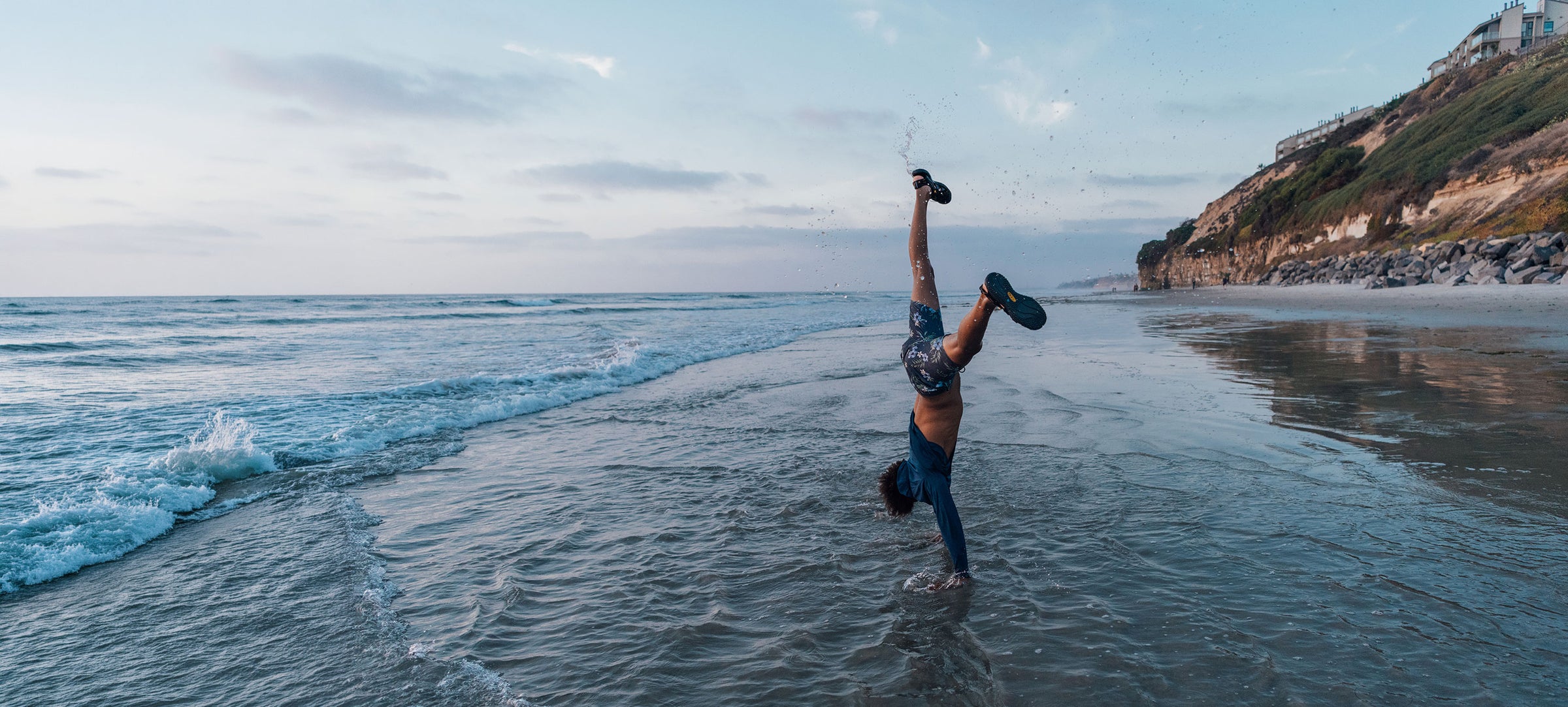 Person doing a handstand in the water at the beach with a scenic background