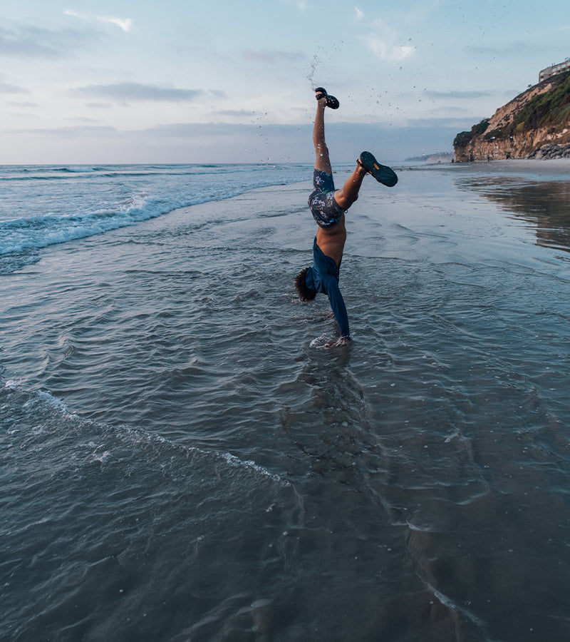 Person doing a handstand in the water on a beach with a scenic background