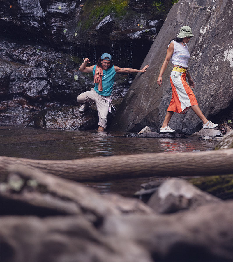 Two people navigating a rocky stream with large boulders and water.