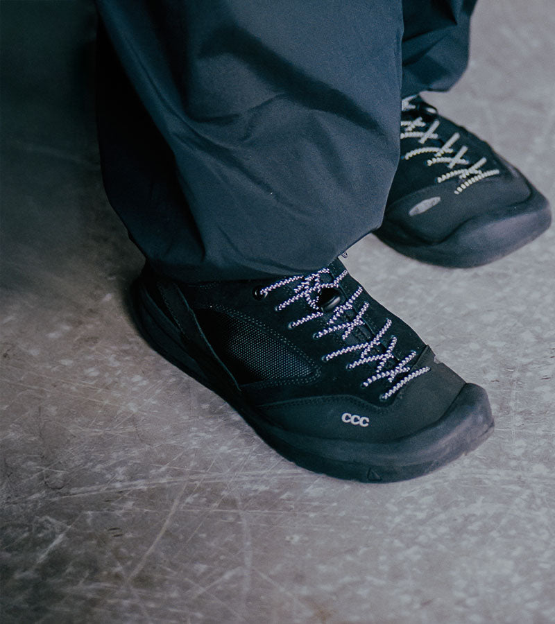 Black hiking boots with white laces worn by a person on a concrete floor.