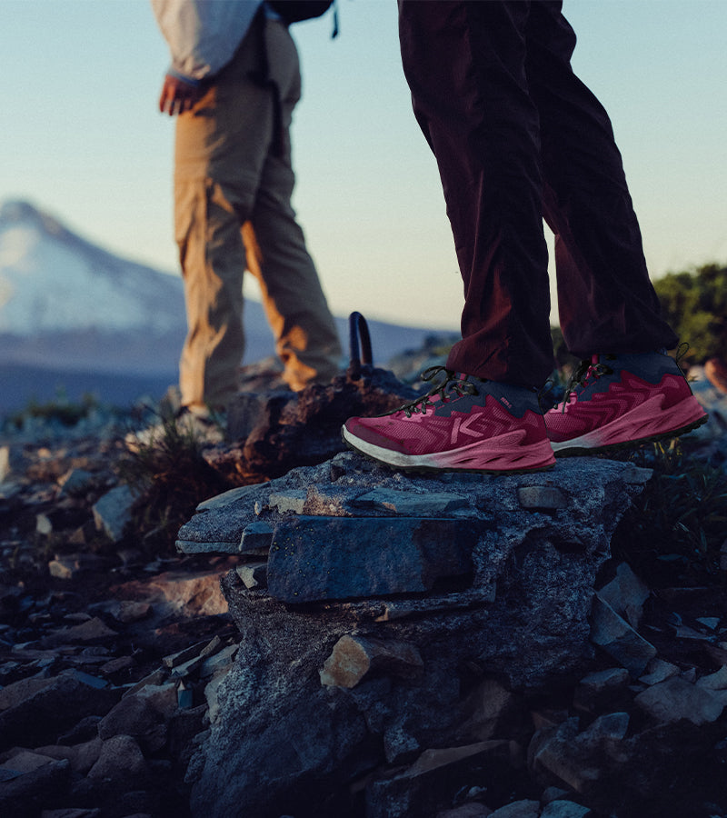 Person wearing pink hiking shoes on a rocky mountain trail with another person in the background.
