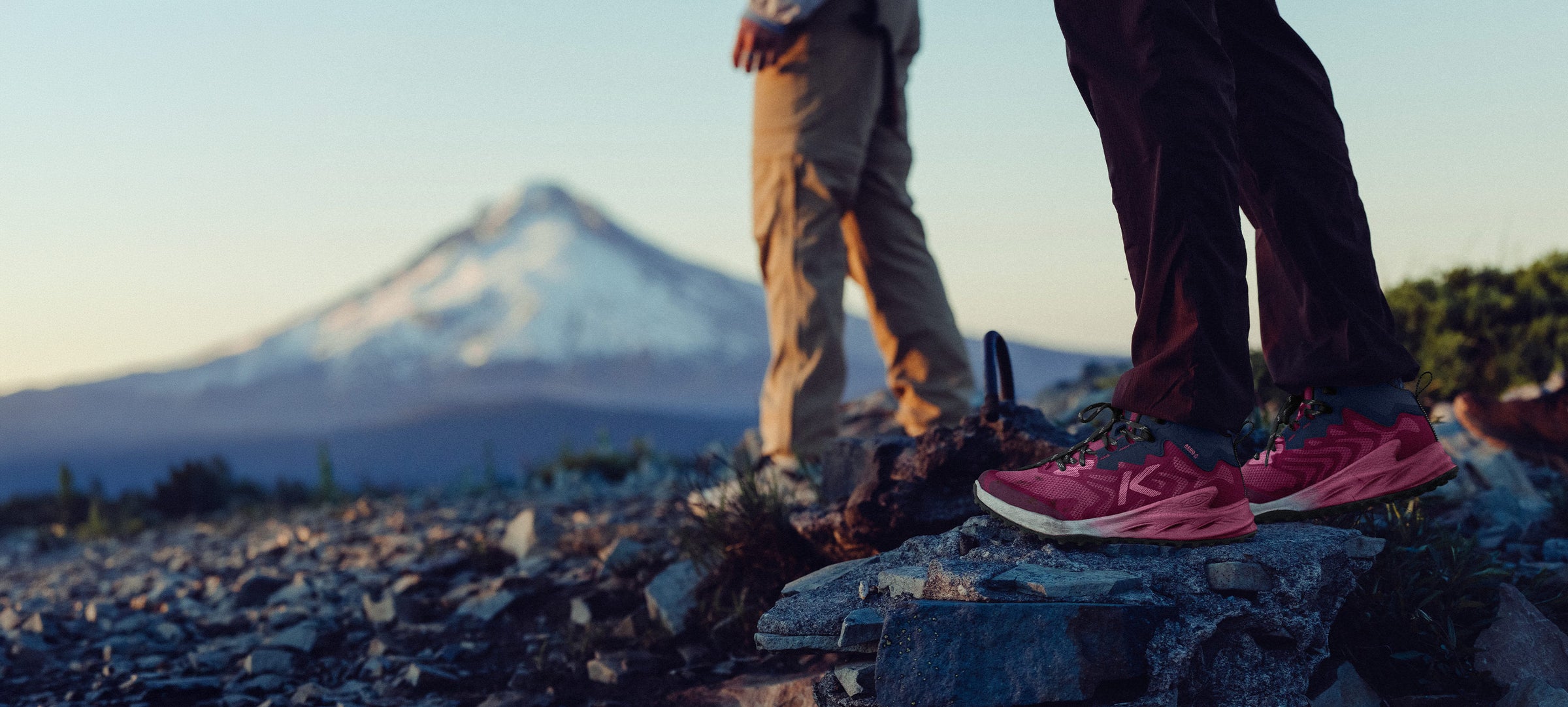 Two people standing on a rocky outcrop with a mountain in the background