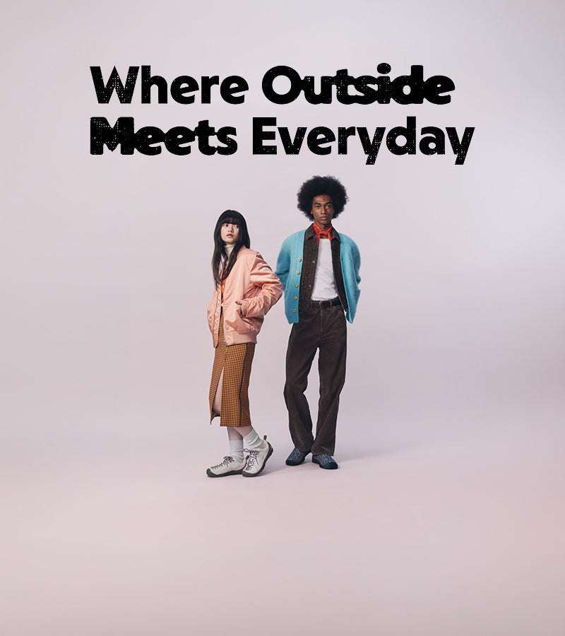 Two models standing against a light gray studio background with the text 'Where Outside Meets Everyday' at the top. The model on the left wears a peach jacket and brown skirt, and the model on the right wears a light blue jacket, brown vest and trousers, white shirt, and red neck scarf.