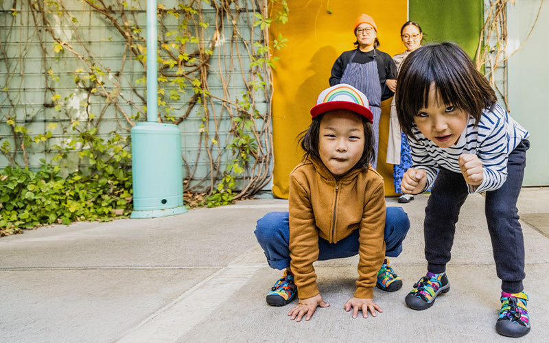 Two children crouching on a sidewalk with a colorful background