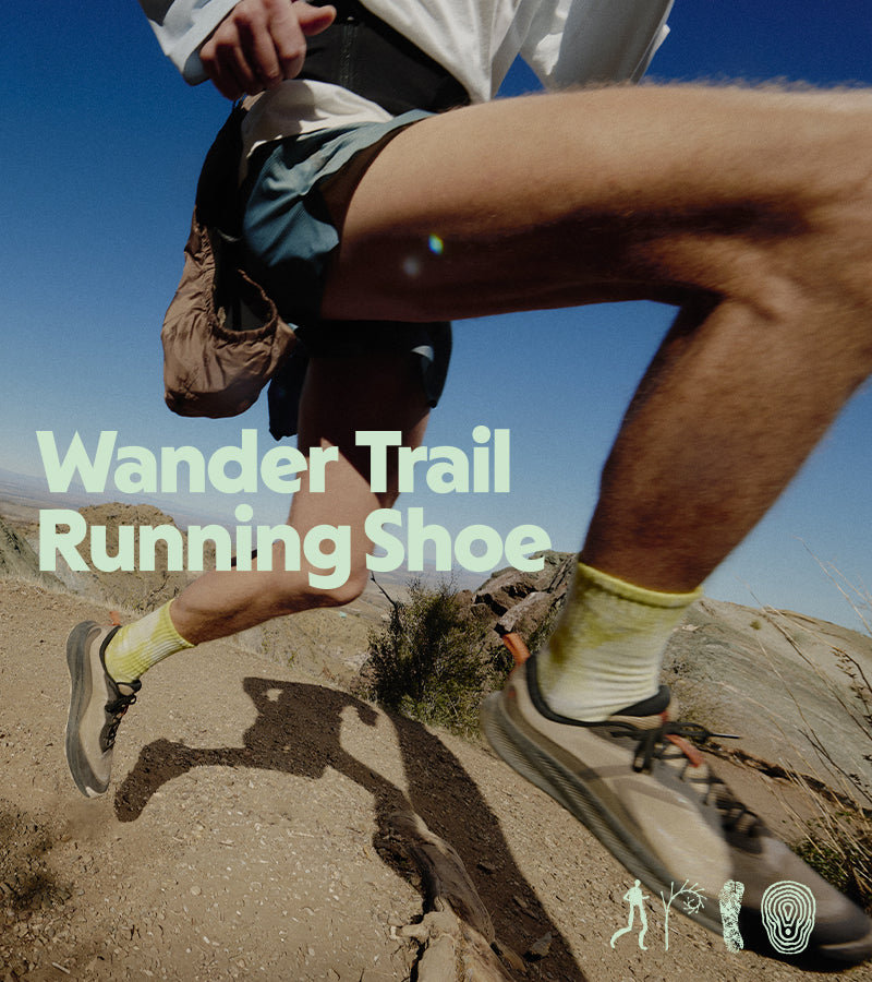 A close-up action shot of a trail runner's legs and shoes running on a sandy desert trail under a blue sky, with the text 'Wander Trail Running Shoe' overlaid on the image.