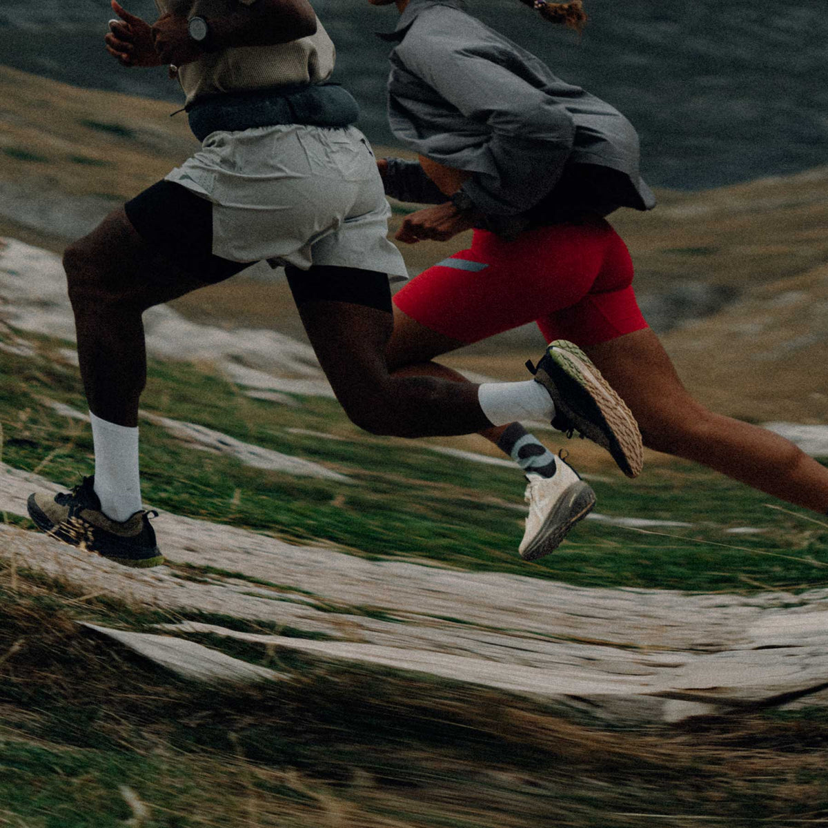 Two runners in athletic gear running on a trail with a mountainous background