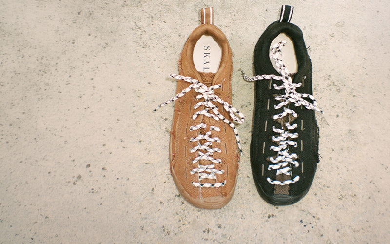 KEEN Jasper Split one in tan leather and one in black suede, both featuring unique braided laces, laid flat on a textured concrete surface.