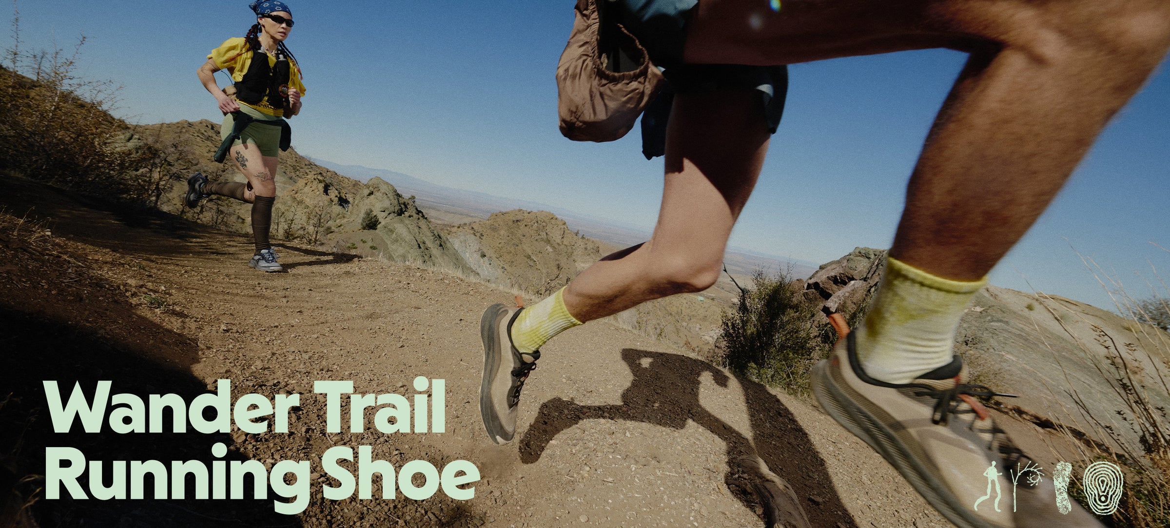 Trail running shoes in action on a rocky desert mountain trail, with a close-up of a runner's legs in the foreground and another runner visible in the background. Text overlay reads 'Wander Trail Running Shoe'.